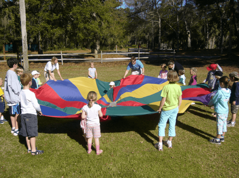 Children engage in a playful activity with a vibrant parachute at a park, as part of the Visit Kiawah Island Guide for family-friendly programs.