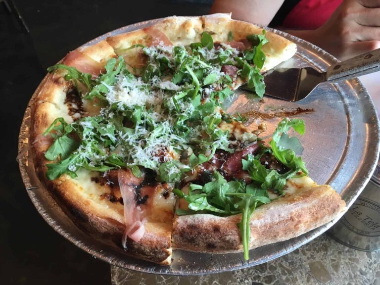 A gourmet pizza topped with arugula and shaved cheese from La Tela Pizzeria on Kiawah Island, highlighting the island's Italian cuisine offerings.