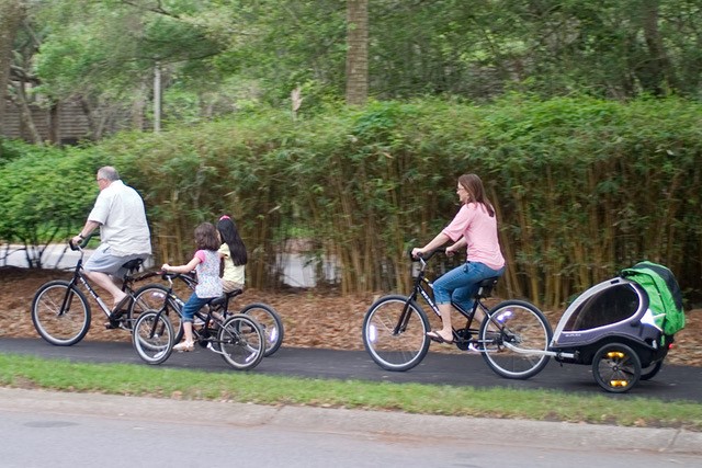 A family enjoys a bike ride on a lush trail, a testament to Kiawah Island's commitment to green transportation highlighted in the guide.