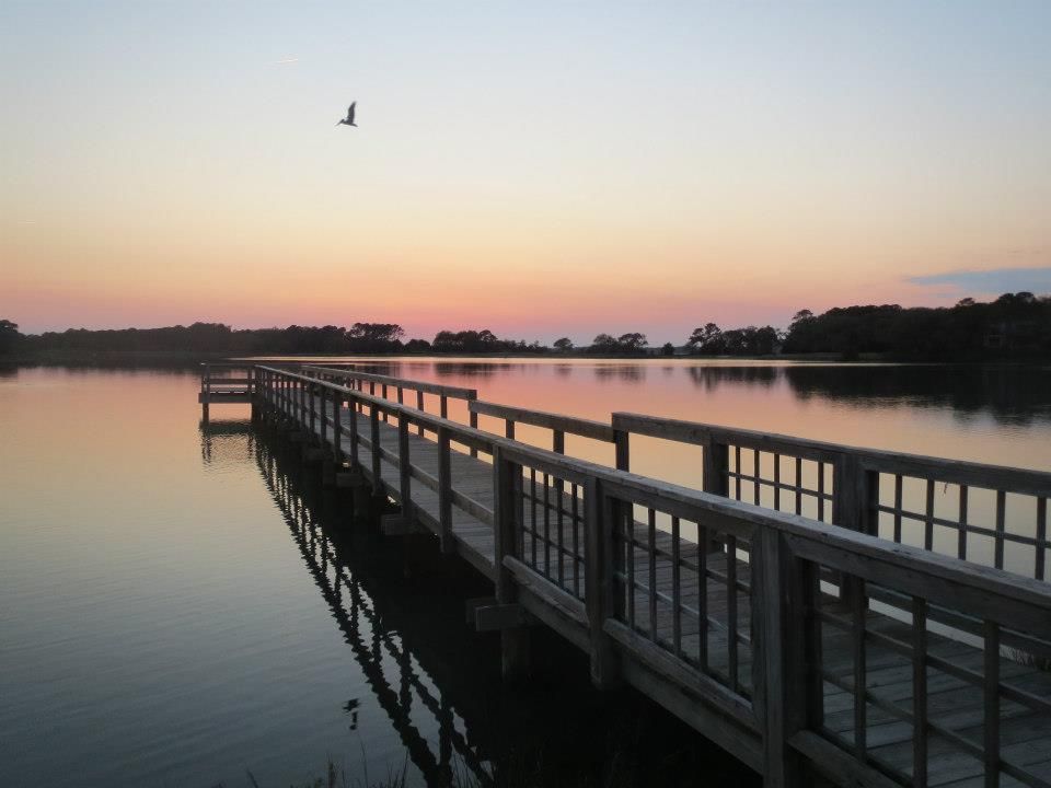 Twilight hues cast over the calm waters at Bass Pond, with the serene Kiawah Island fishing dock extending into the water, from the Visit Kiawah Island Guide.