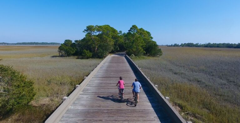 Two people cycling over a wooden bridge surrounded by marshland at Eagle Point.