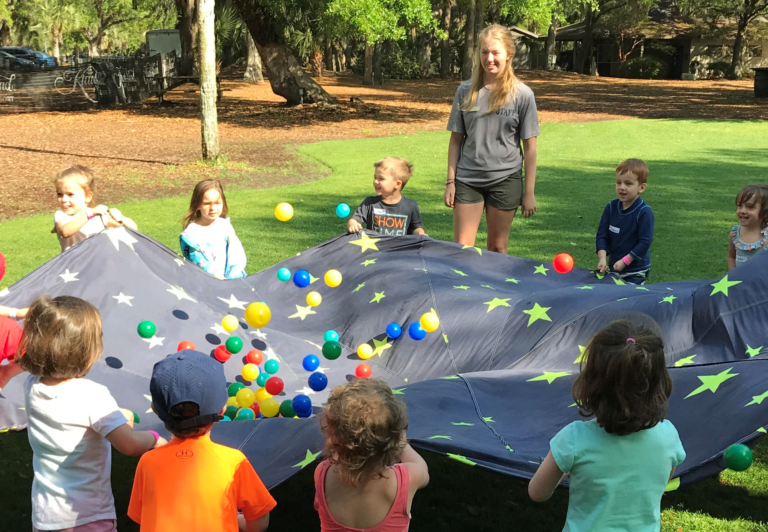 Energetic children engaging in parachute play at Kamp Kiawah Children's Program, a favorite for Kiawah Island teens and younger kids.