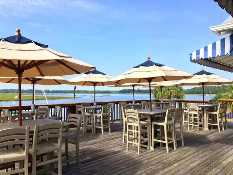 The serene outdoor dining area of Salty Dog Cafe at Kiawah Island, featuring ample seating under beige umbrellas with a picturesque marshland backdrop.